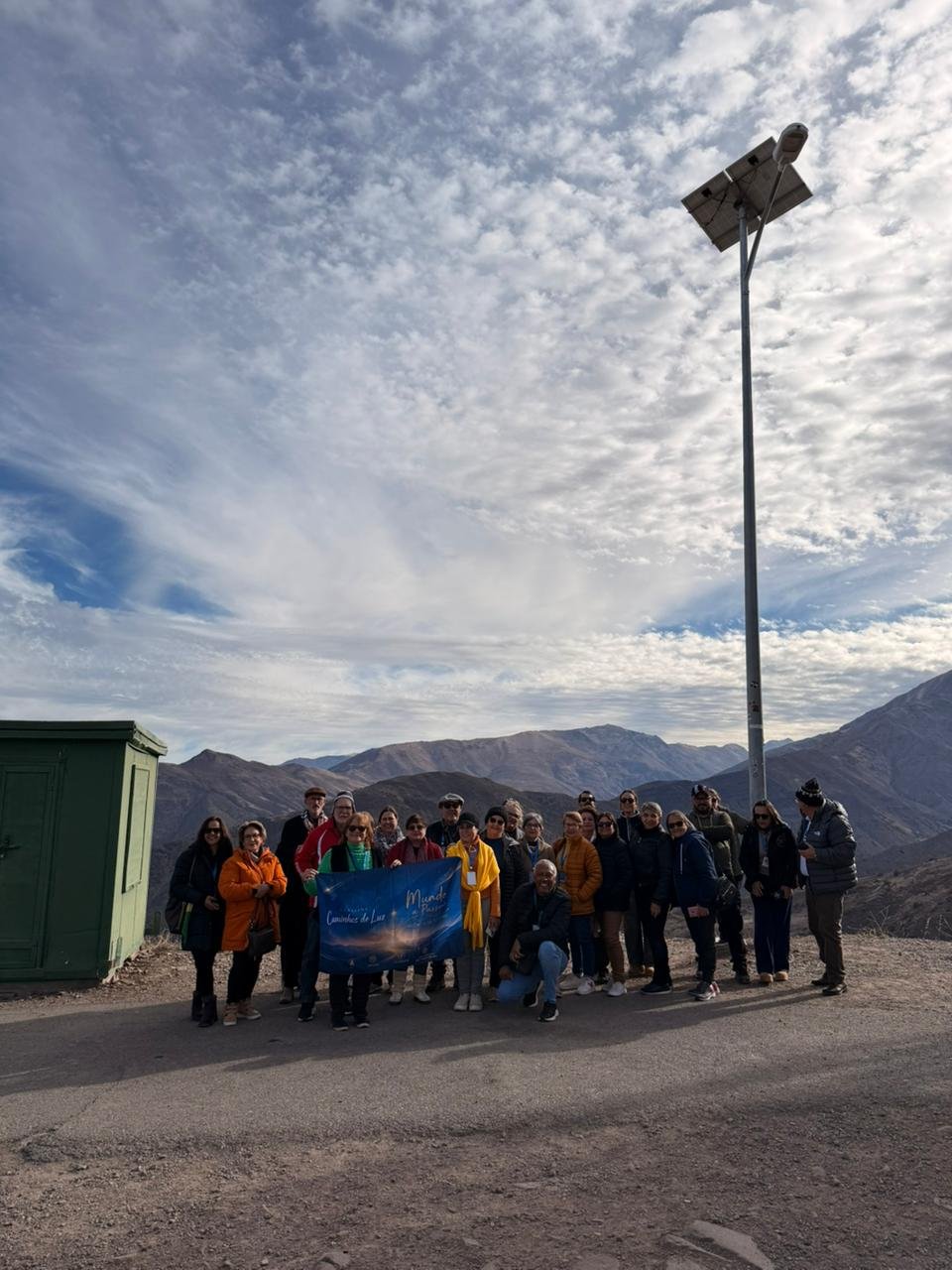 Grupo grande em paisagem de montanha com céu azul, todos em primeiro plano