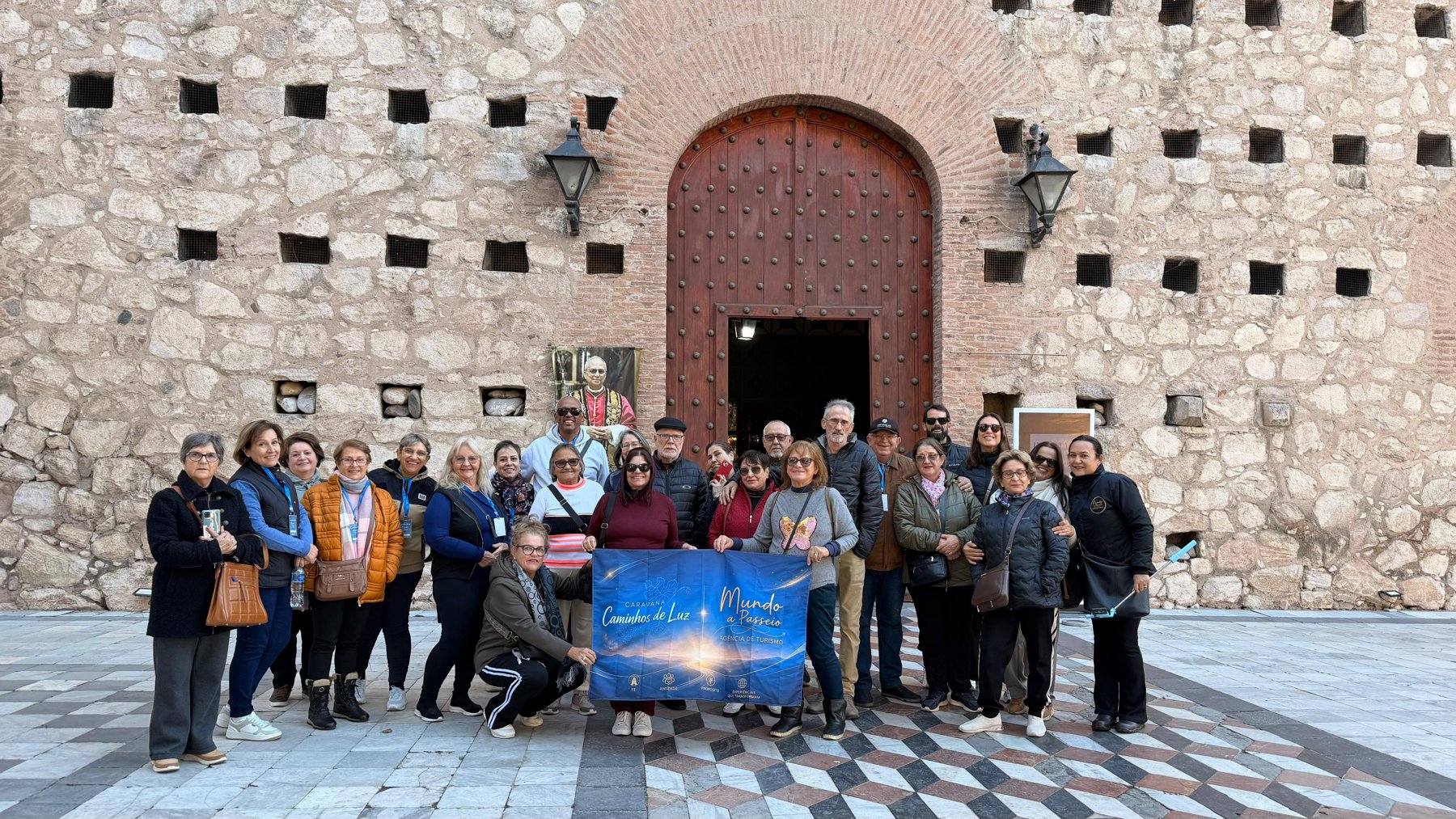 Grupo grande com bandeira em frente a edifício histórico de fachada clara, horizontal, bem iluminado