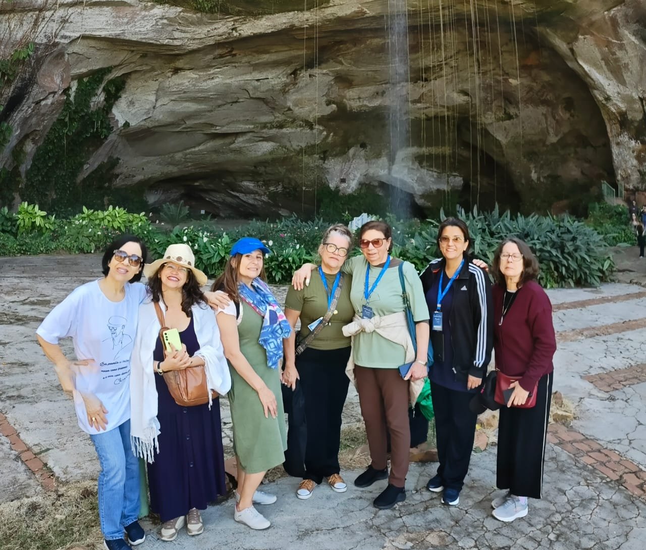 Grupo em frente a formação rochosa com entrada de caverna, exterior com boa iluminação