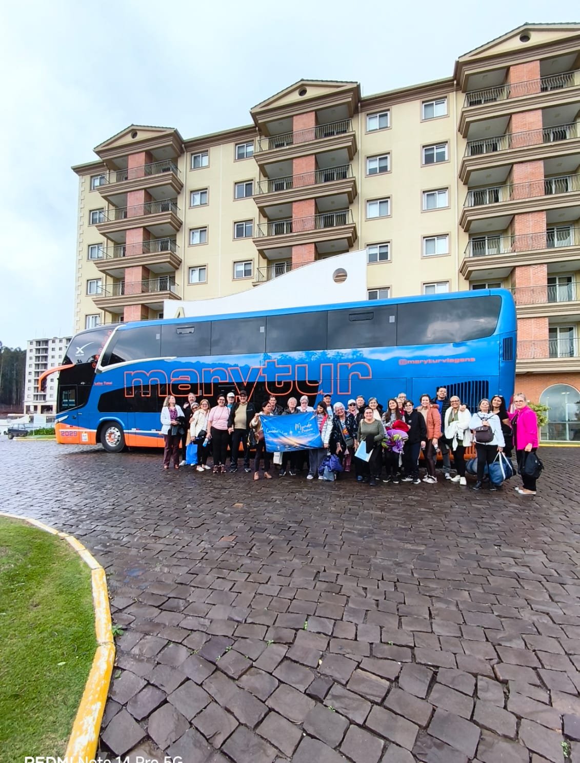 Grupo em frente ao ônibus da agência, pátio com edifício ao fundo, luz natural boa