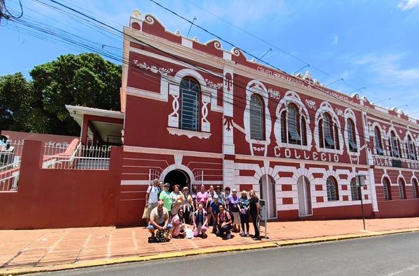 Grupo posando na calcada em frente a fachada historica vermelha e branca