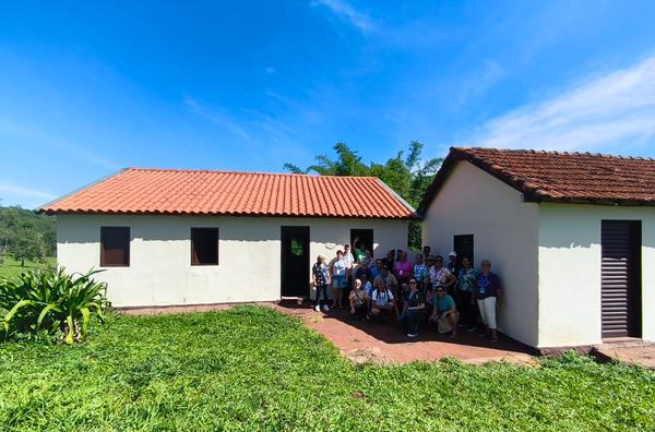 Grupo posando em frente a conjunto de casaroes brancos com telhado de barro