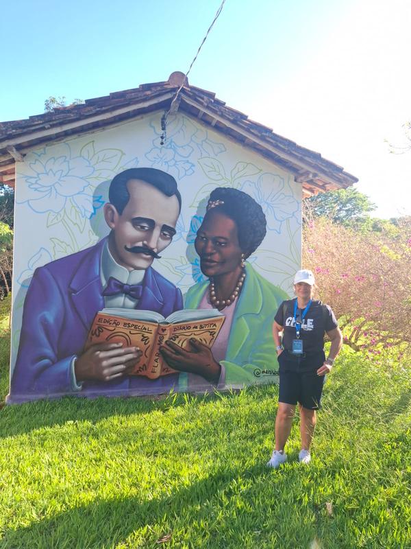 Pessoa posando em frente a mural pintado com casal segurando um livro