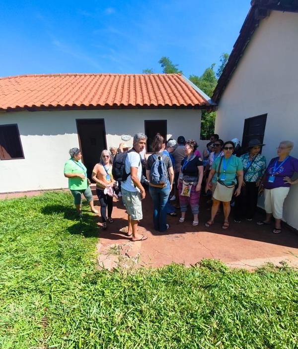Grupo reunido perto da entrada de casarao branco durante visita