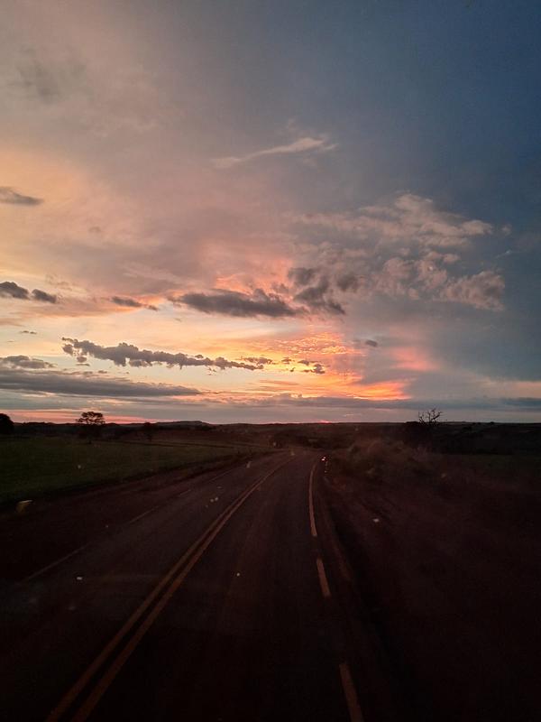Estrada deserta ao entardecer com o ceu alaranjado ao fundo