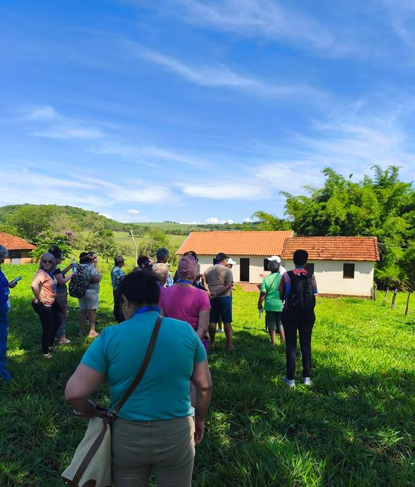 Grupo em campo verde com casarao de telhado de barro ao fundo