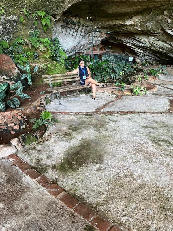 Visitante sentada em banco dentro da gruta, na Caravana Minas Espirita de novembro de 2025