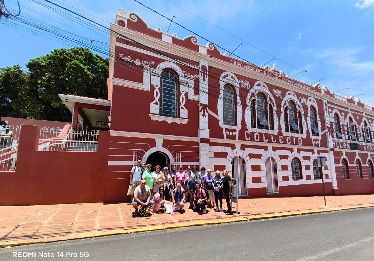 Grupo em frente a construção histórica vermelha com arquitetura colonial, luz clara, horizontal