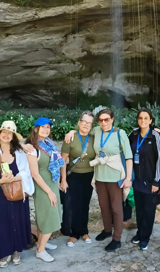 Grupo em frente a formação rochosa com entrada de caverna, exterior com boa iluminação