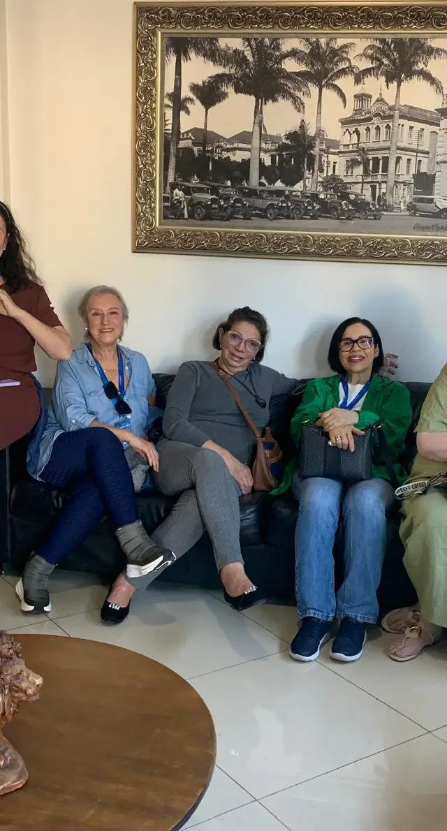 Grupo de aproximadamente 15 pessoas em espaço com fotos nas paredes, ambiente de museu