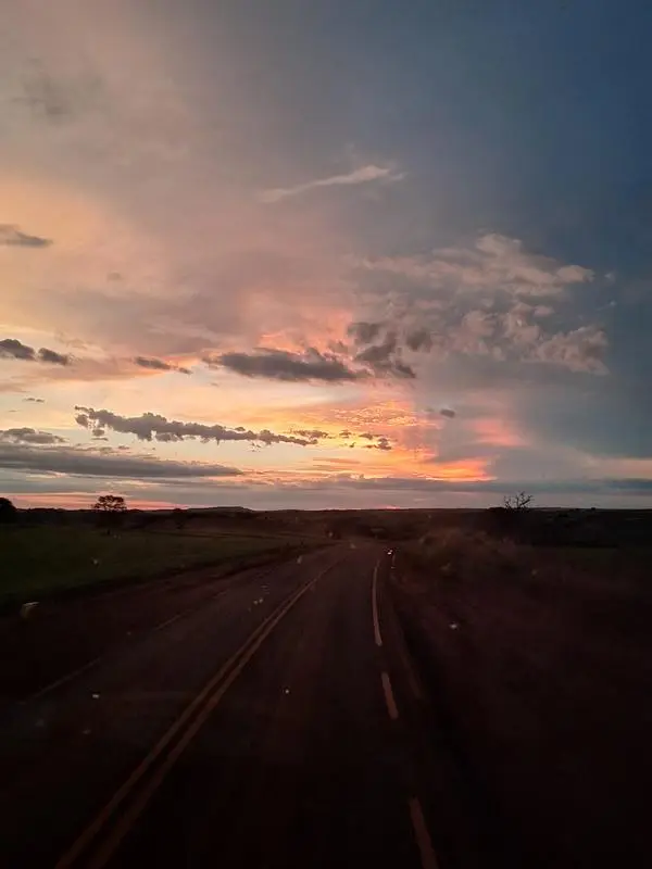 Estrada deserta ao entardecer com o ceu alaranjado ao fundo