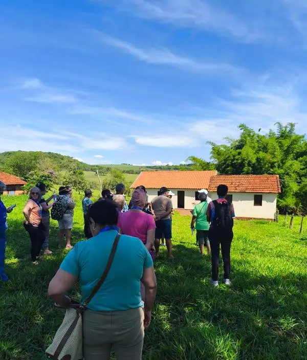 Grupo em campo verde com casarao de telhado de barro ao fundo