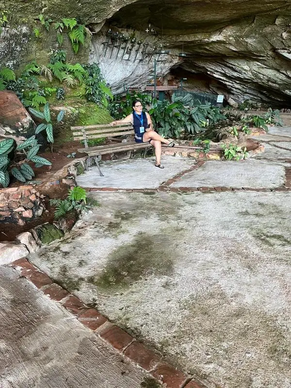 Visitante sentada em banco dentro da gruta, na Caravana Minas Espirita de novembro de 2025